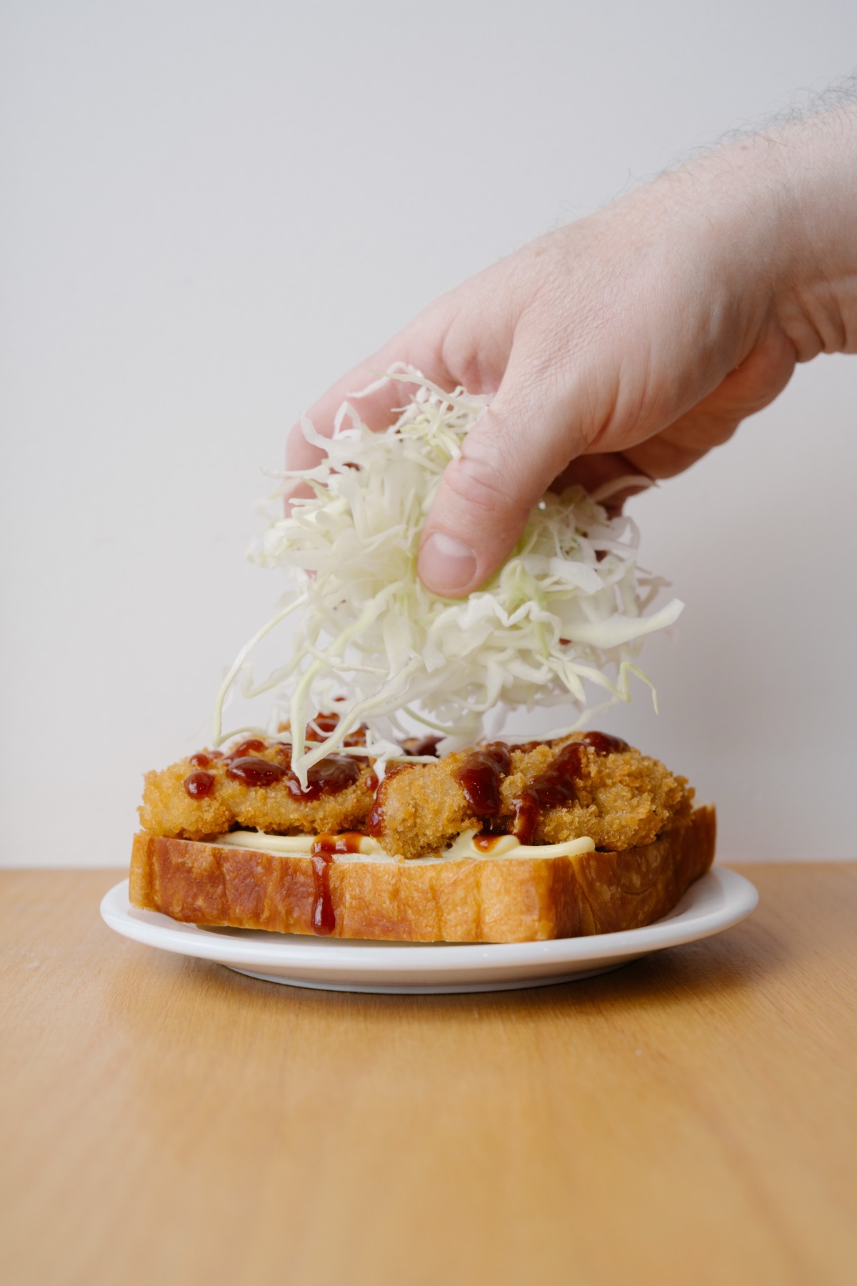 A handful of shredded cabbage landing on a sauced katsu cutlet